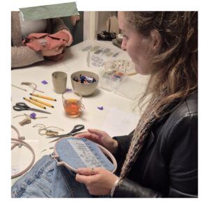 Deelnemer borduurt een bloemenmotief op een spijkerjack tijdens workshop Borduren op Kleding in Friesland