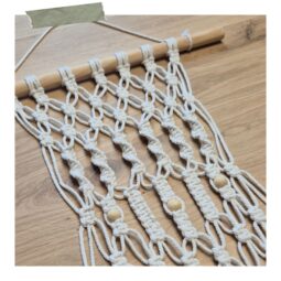 Close-up van ecru macramékoord en houten kralen in een wandhanger tijdens een creatieve workshop